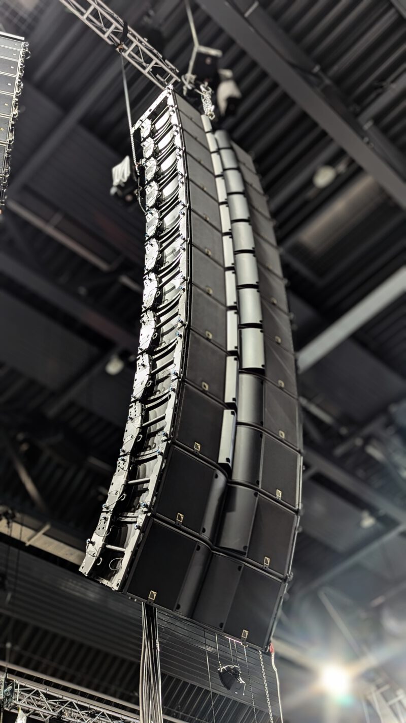 Geflogenes Line-Array-Lautsprechersystem in einer Veranstaltungshalle, montiert an einer Traverse und für professionelle Beschallung ausgerichtet.