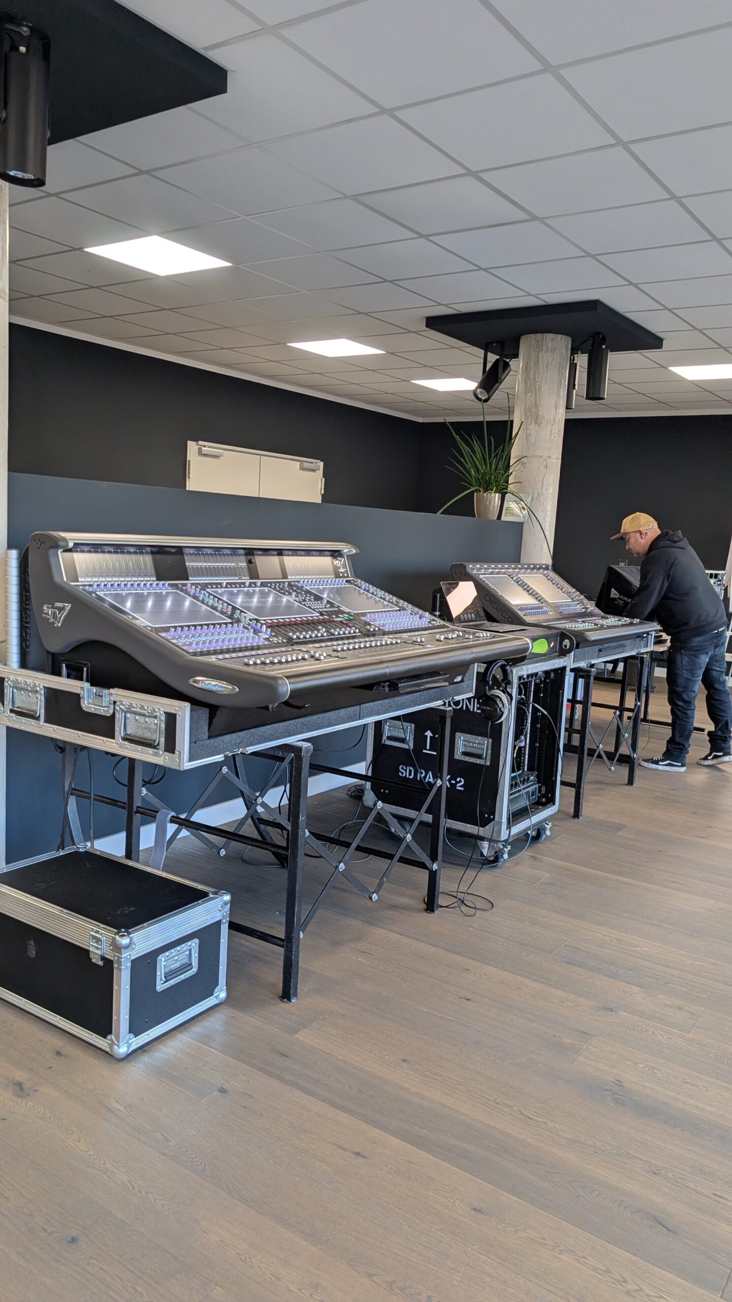 Zwei große digitale DiGiCo SD7 Mischpulte in einem modernen Studio auf Holzfußboden. Ein Mann arbeitet an einem der Pulte, der Raum ist hell beleuchtet.