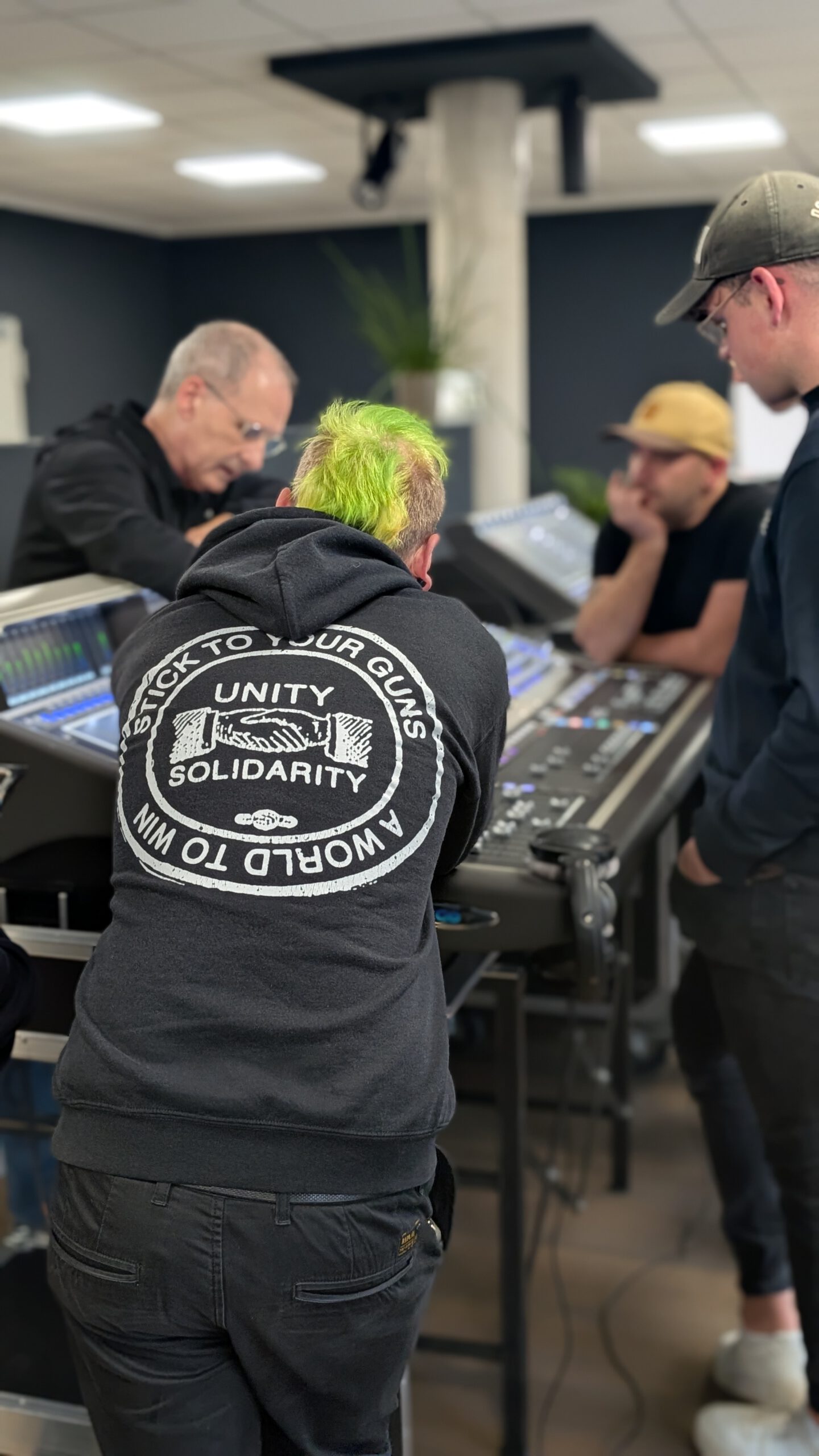 Mehrere Tontechniker arbeiten gemeinsam an einem digitalen Mischpult in einem modernen Studio. Der Fokus liegt auf der Zusammenarbeit und technischen Abstimmung.