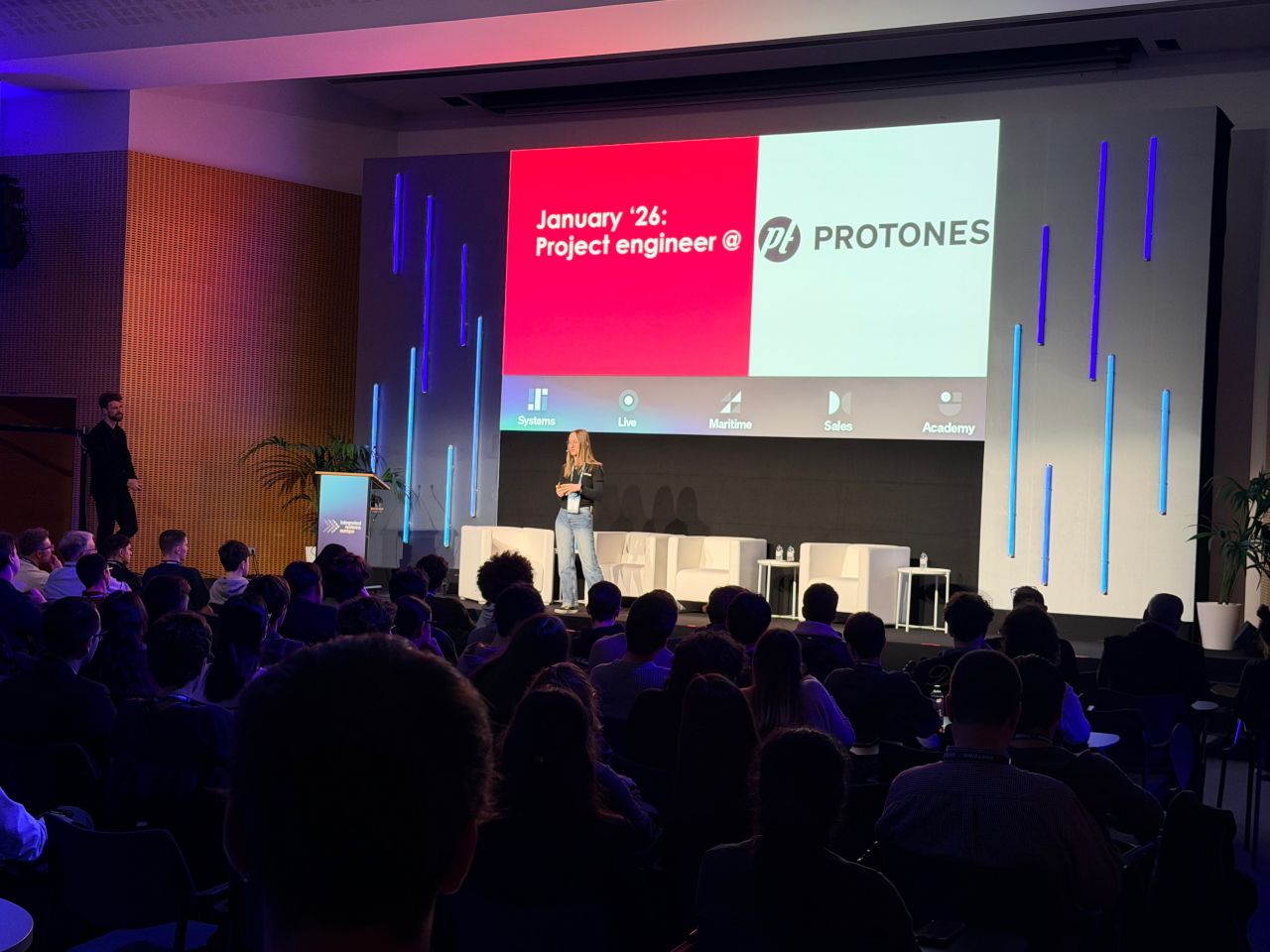 Jasmin Thieme spricht auf der Bühne des AV Career Day bei der ISE 2026 vor großem Publikum, im Hintergrund eine PROTONES Präsentationsfolie.