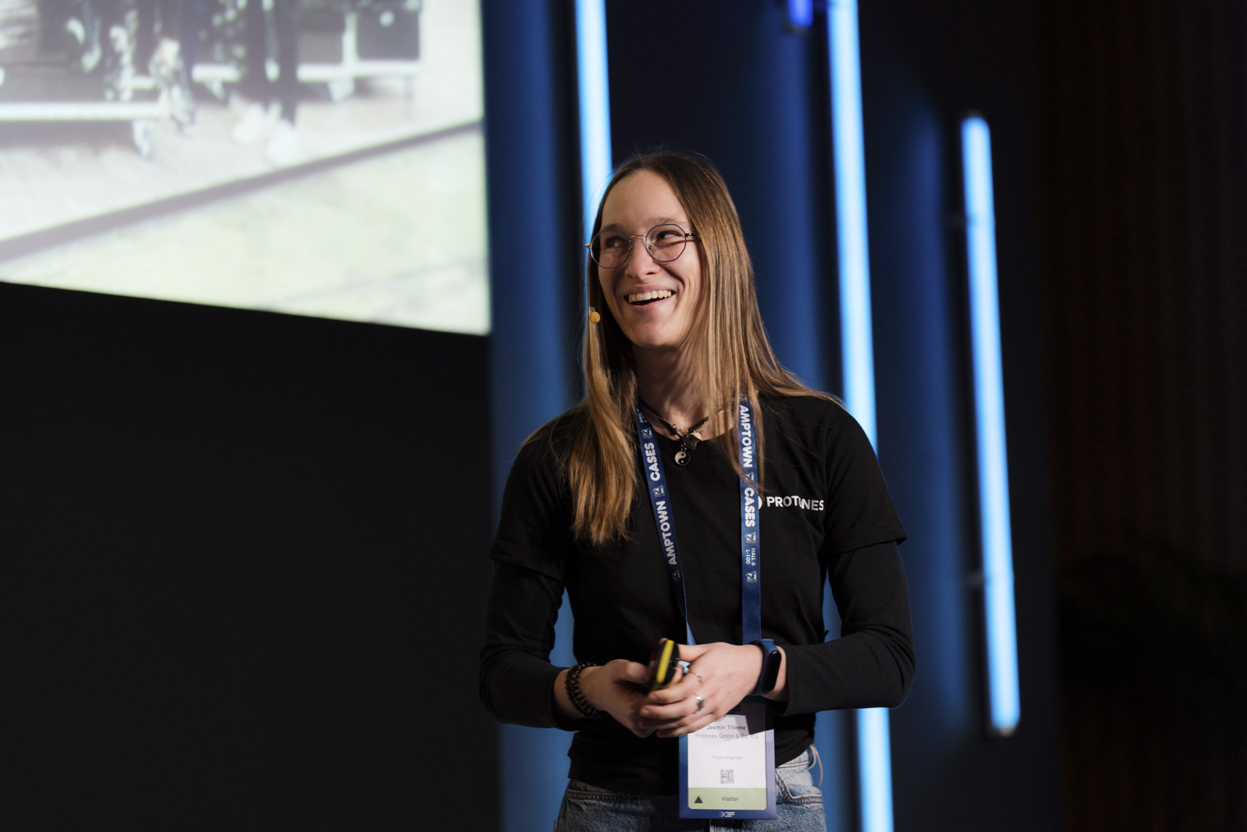 Jasmin Thieme während ihres Vortrags auf der ISE 2026, lächelnd mit Headset-Mikrofon und PROTONES Branding.